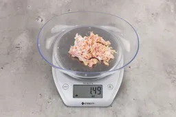 1.49 ounces of crushed chicken bone and cartilage, and shredded tendon and meat on digital scale on granite-looking top. 
