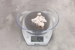 0.98 ounces of shredded fatty tissue and broken cartilage from chicken scraps on digital scale on granite-looking top.