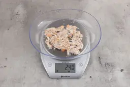 2.4 ounces of visible pin bones in a mass of raw meat and skin from fish scraps on digital scale on granite-looking top.