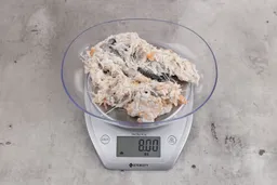 8 ounces of visible pin bones in a mass of raw meat and skin from fish scraps on digital scale on granite-looking top.