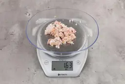 1.63 ounces of ground chicken scraps from garbage disposal, displayed on digital scale, placed on granite-looking table. Mess of shredded tendons and pieces of shredded bones.
