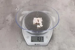 0.37 ounces of ground chicken scraps from a garbage disposal, displayed on digital scale, placed on granite-looking table. Mess of soft tissue and pieces of shredded cartilage.