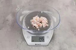 1.45 ounces of ground chicken scraps from garbage disposal, displayed on digital scale, placed on granite-looking table. Mess of shredded soft tissue and few pieces of shredded bones.