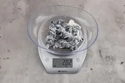 2.02 ounces of ground fish scraps from a garbage disposal, displayed on digital scale, placed on granite-looking table. Mess of shredded fish backbone and skin.