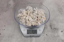 5.56 ounces of ground fish scraps from garbage disposal, displayed on digital scale, placed on granite-looking table. Few pin bones among a mess of raw fibrous tissue.