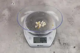 0.06 ounces of ground products from garbage disposal, displayed on digital scale, placed on granite-looking table. Shredded fish vertebrae and pieces of dietary fiber.
