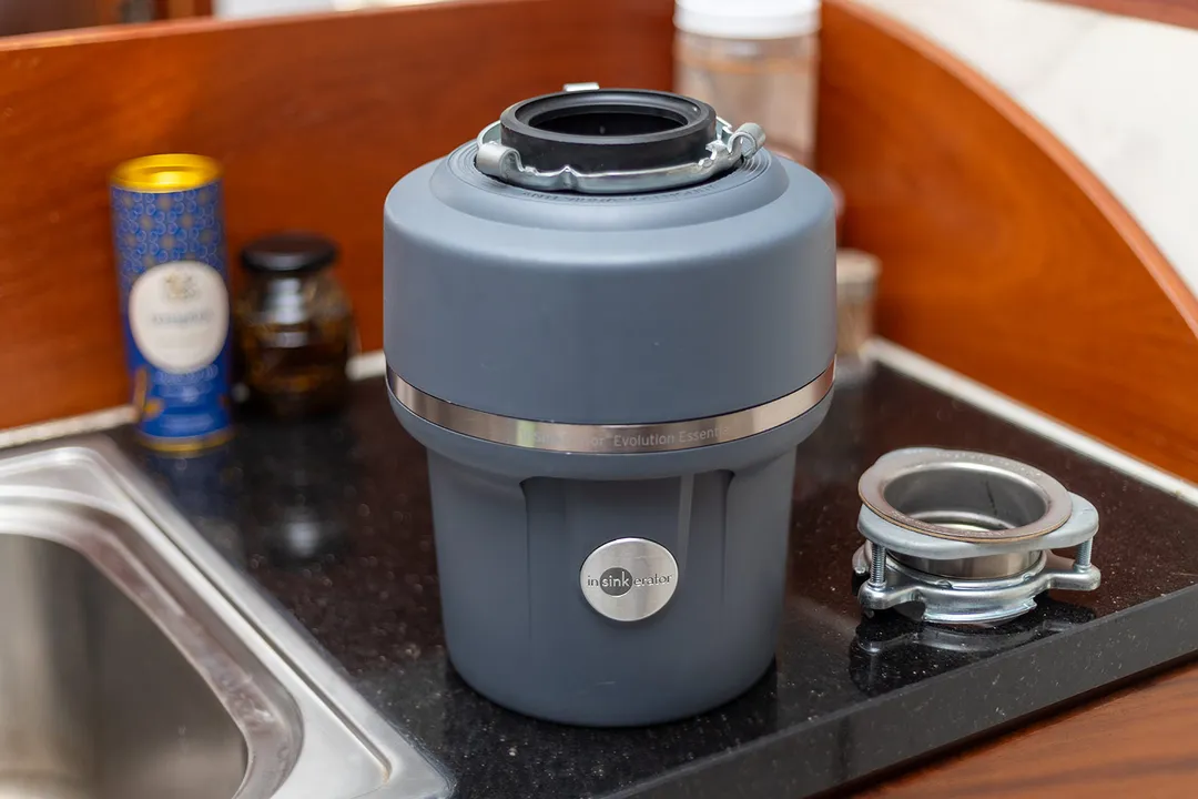 InSinkErator Evolution Essential XTR 3/4-Horsepower Garbage Disposal sitting on a kitchen countertop, next to the 3-bolt mounting assembly.