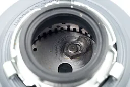 Top view through collar of InSinkErator Essential XTR 3/4-hp garbage disposal into grinding chamber after testing. Highlighting layout of grinding components, showing swivel impellers, flywheel, and grater/grinder ring.