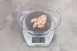 1.01 ounces of ground chicken scraps from garbage disposal, displayed on digital scale, placed on granite-looking table. Mess of shredded tendons and pieces of shredded bones.