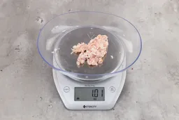 1.01 ounces of ground chicken scraps from garbage disposal, displayed on digital scale, placed on granite-looking table. Mess of shredded tendons and pieces of shredded bones.