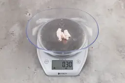 0.3 ounces of ground chicken scraps from a garbage disposal, displayed on digital scale, placed on granite-looking table. Mess of soft tissue and pieces of shredded cartilage.
