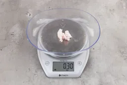 0.3 ounces of ground chicken scraps from a garbage disposal, displayed on digital scale, placed on granite-looking table. Mess of soft tissue and pieces of shredded cartilage.