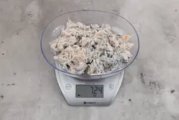 7.24 ounces of ground fish scraps from garbage disposal, displayed on digital scale, placed on granite-looking table. Broken fish bones among a mess of raw fibrous tissue.