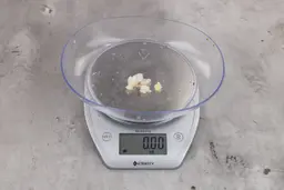 Almost 0 ounces of ground products from garbage disposal, displayed on digital scale, placed on granite-looking table. Pieces of shredded dietary fiber.