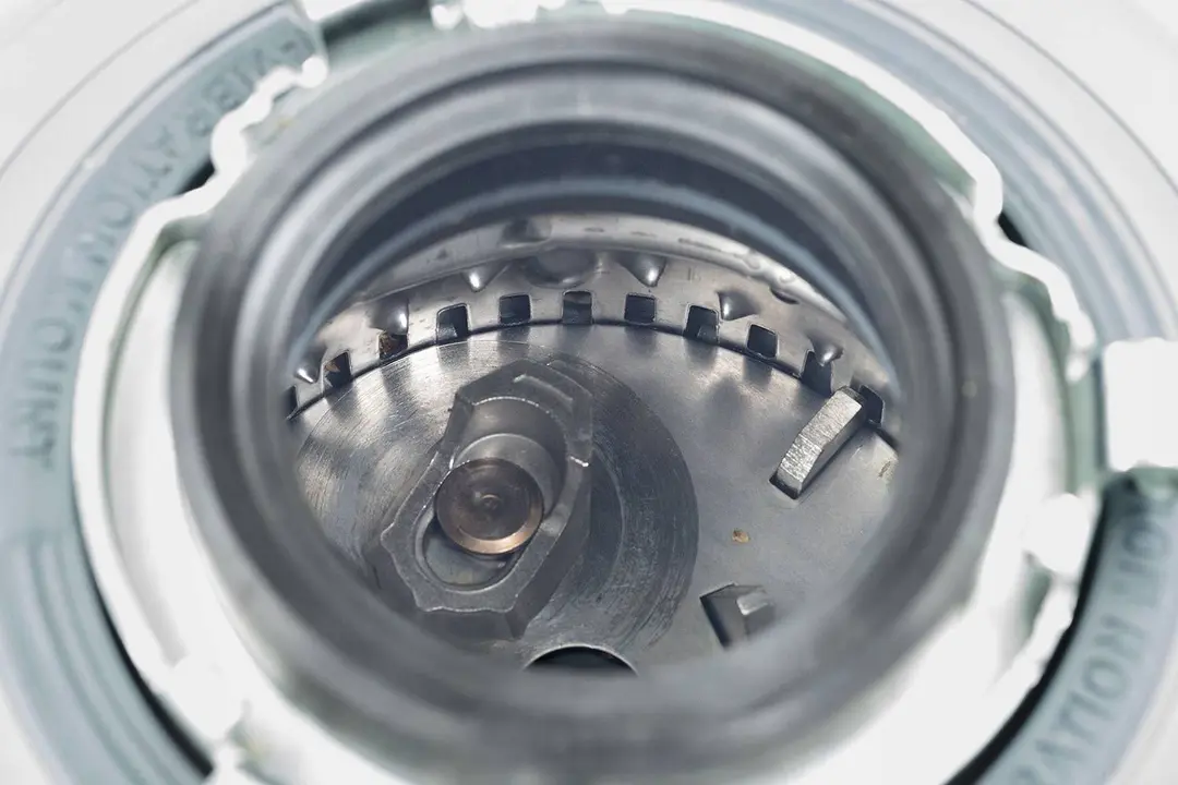 Top view through collar of InSinkErator Evolution 1-hp garbage disposal into chamber after testing. Looking at layout of grinding components, showing swivel impellers, flywheel, and grater/grinder ring.