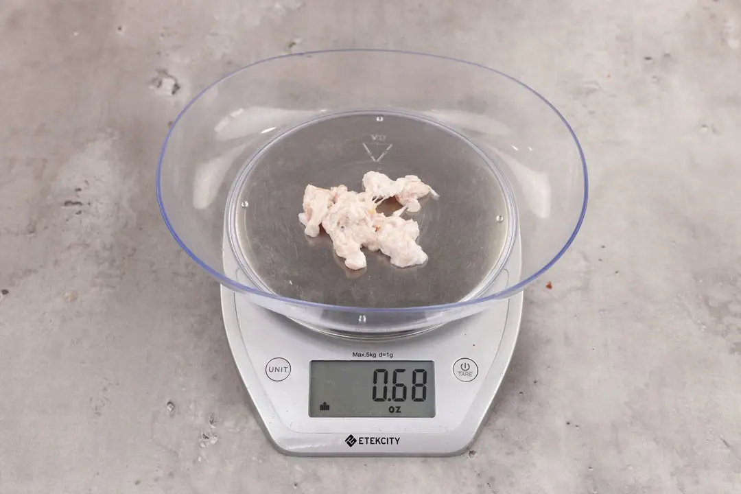 0.68 ounces of ground chicken scraps from garbage disposal, displayed on digital scale, placed on granite-looking table. Mess of shredded soft tissue and few pieces of shredded bones.