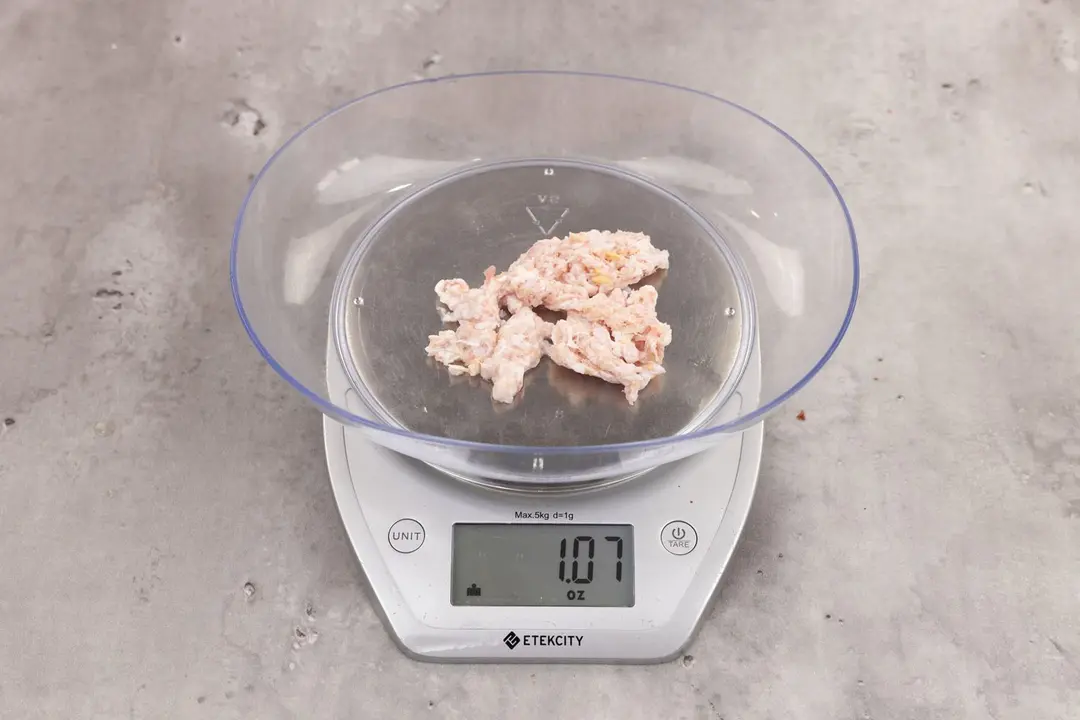 1.07 ounces of ground chicken scraps from garbage disposal, displayed on digital scale, placed on granite-looking table. Mess of fibrous soft tissue and pieces of shredded bones.