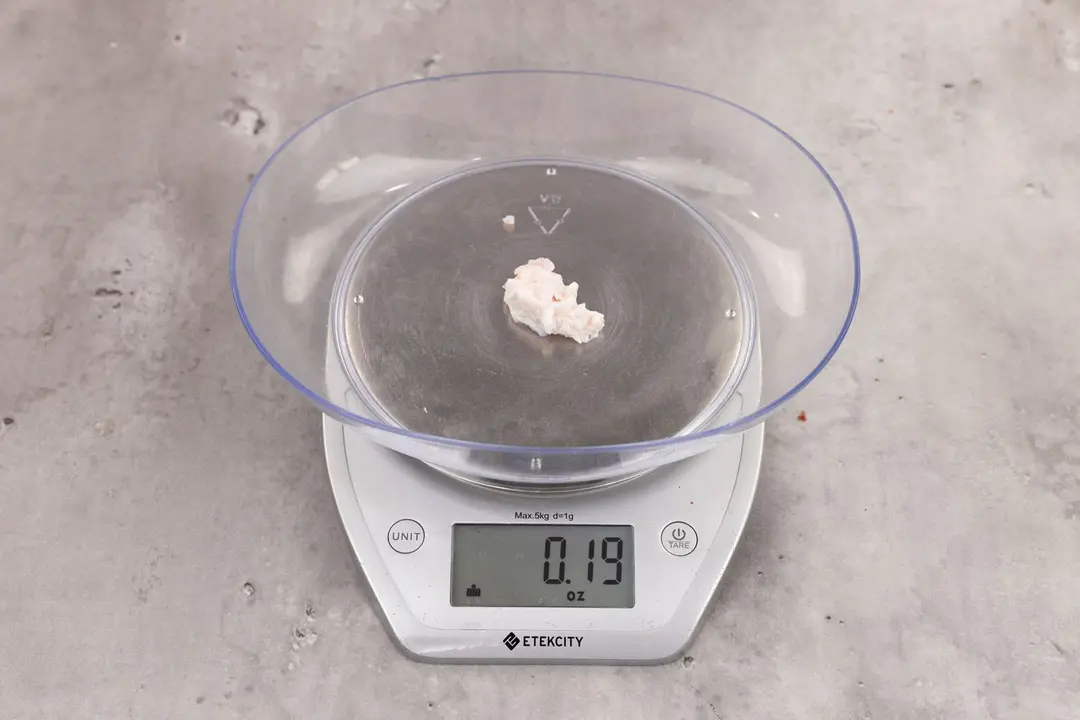 0.19 ounces of ground chicken scraps from garbage disposal, displayed on digital scale, placed on granite-looking table. Small mess of soft tissue and pieces of shredded cartilage.