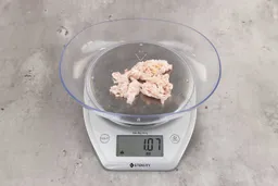 1.07 ounces of ground chicken scraps from a garbage disposal, displayed on a digital scale, placed on a granite-looking table. Mess of fibrous soft tissue and pieces of shredded bones.