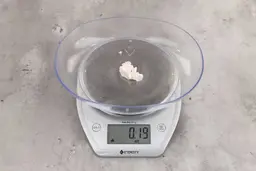 0.19 ounces of ground chicken scraps from a garbage disposal, displayed on a digital scale, placed on a granite-looking table. Small mess of soft tissue and pieces of shredded cartilage.