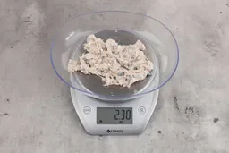 2.3 ounces of ground fish scraps from a garbage disposal, displayed on a digital scale, placed on a granite-looking table. Mess of assorted shredded bones and raw fibrous tissue.