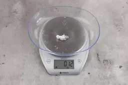 0.12 ounces of ground fish scraps from a garbage disposal, displayed on a digital scale, placed on a granite-looking table. Small mess of shredded fish backbone and skin.