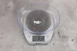 0.12 ounces of ground fish scraps from a garbage disposal, displayed on a digital scale, placed on a granite-looking table. Small mess of shredded fish backbone and skin.
