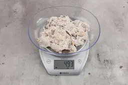 4.93 ounces of ground fish scraps from a garbage disposal, displayed on a digital scale, placed on a granite-looking table. Visible pin bones among a mess of raw fibrous tissue.