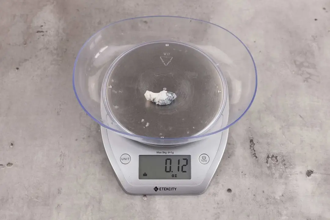 0.12 ounces of ground fish scraps from a garbage disposal, displayed on digital scale, placed on granite-looking table. Small mess of shredded fish backbone and skin.