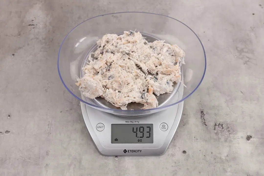 4.93 ounces of ground fish scraps from garbage disposal, displayed on digital scale, placed on granite-looking table. Visible fish pin bones among mess of uncooked fibrous tissue and assorted shredded fish bones.