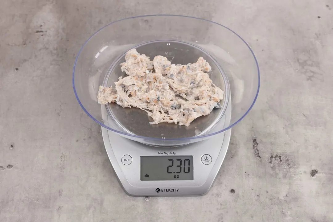 2.3 ounces of ground fish scraps from garbage disposal, displayed on digital scale, placed on granite-looking table. Mess of assorted shredded fish bones and uncooked fibrous tissue.
