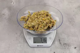 7.16 ounces of ground products from a garbage disposal, displayed on a digital scale, placed on a granite-looking table. Mess of assorted scraps, including fibers, bones, etc.