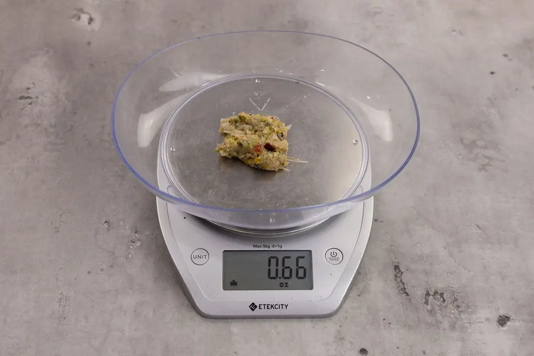 0.66 ounces of ground products from garbage disposal, displayed on digital scale, placed on granite-looking table. Visible fish pin bones in mess of assorted scraps.