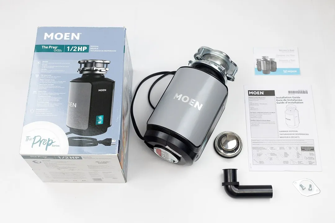 Moen GX50C 1/2 Horsepower Garbage Disposal with EZ Mount assembly on top, next to its box, user manual, registration slip, sink stopper, elbow tube, and a set of flange and bolts.