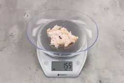 1.55 ounces of ground chicken scraps from garbage disposal, displayed on digital scale, placed on granite-looking table. Mess of shredded tissues and shredded bones.