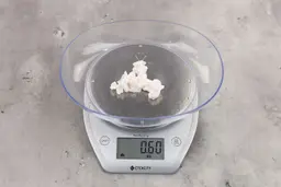 0.6 ounces of ground chicken scraps from a garbage disposal, displayed on digital scale, placed on granite-looking table. Mess of soft tissue and pieces of shredded cartilage.