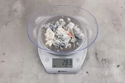2.83 ounces of ground fish scraps from a garbage disposal, displayed on digital scale, placed on granite-looking table. Mess of shredded fish backbone and skin.