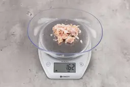 1.62 ounces of shredded soft tissue and pieces of shredded chicken bone, on digital scale, on granite-looking top.