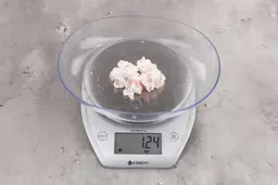 1.24 ounces of shredded soft stringy tissue and cartilage from chicken scraps, on digital scale, on granite-looking top.