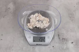 2.02 ounces of shredded bones and fibrous tissue from fish scraps, on digital scale, placed on granite-looking top.