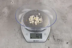 0.23 ounces of shredded pieces of fish backbone, dietary fibers, and fish meat, on digital scale, on granite-looking top.