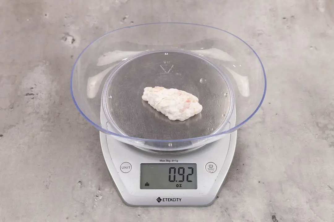 0.92 ounces of ground chicken scraps from garbage disposal, displayed on digital scale, placed on granite-looking table. Mess of shredded soft tissue.