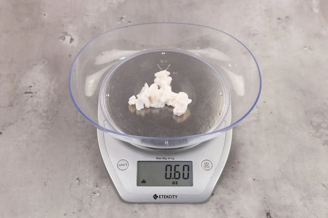 0.6 ounces of ground chicken scraps from garbage disposal, displayed on digital scale, placed on granite-looking table. Pieces of shredded cartilage among mess of soft tissue.