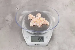 1.59 ounces of shredded soft tissue and pieces of shredded chicken bones, on digital scale, on granite-looking top.