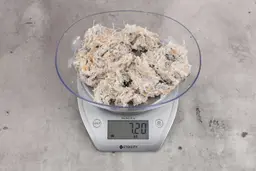 0.14 ounces of shredded soft stringy tissue and cartilage from chicken scraps, on digital scale, on granite-looking top.
