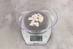 0.84 ounces of fibrous soft tissue and few pieces of shredded chicken bones, on digital scale, on granite-looking top.