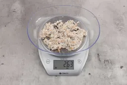 2.63 ounces of shredded bones and fibrous tissue from fish scraps, on digital scale, placed on granite-looking top.