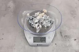 3 ounces of fish vertebrae among mess of shredded fish skin, on digital scale, on granite-looking top.