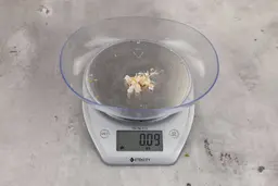 0.09 ounces of shredded pieces of fish backbone, dietary fibers, and fish meat, on digital scale, on granite-looking top.