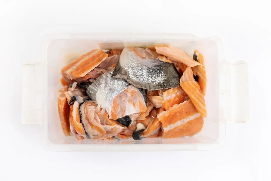 Raw salmon scraps prepared for performance reviewing of best garbage disposals, display in plastic container on white top.